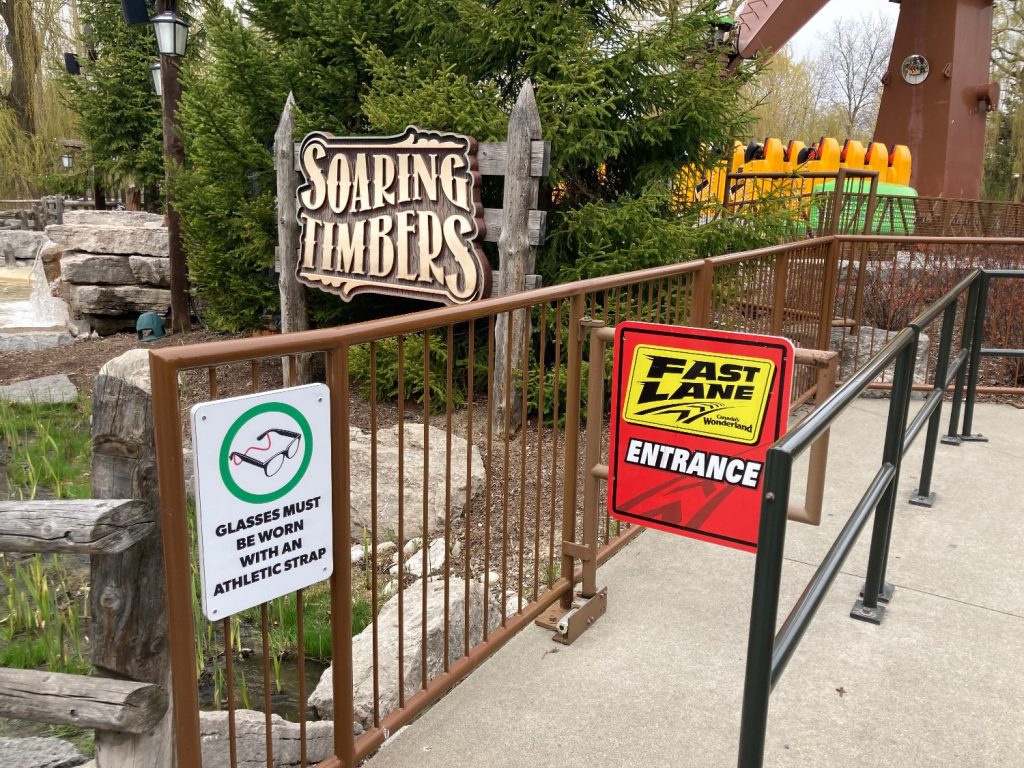 A sign stating glasses must be secured with an athletic strap. Outside of Soaring Timbers, next to the Fast Lane entrance.