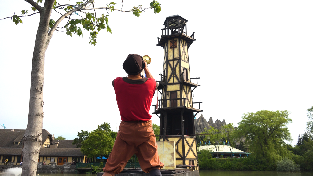 A performer playing a horn in the direction of the Arthur's Baye tower.