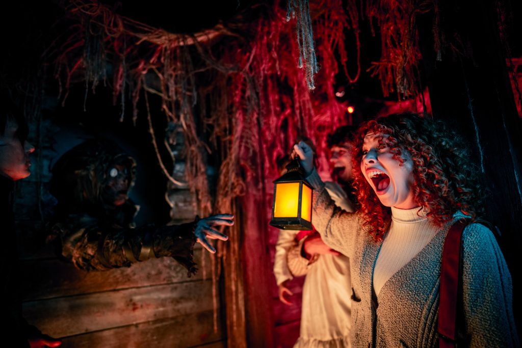 Guests screaming while holding a lantern as a creature reaches out toward them.